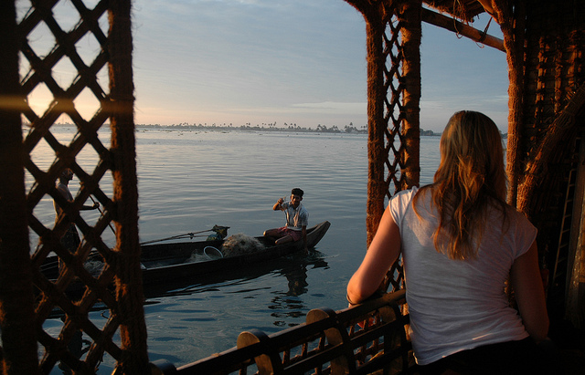 View from inside a houseboat at dawn — a fisherman in a small boat on still water, Alleppey