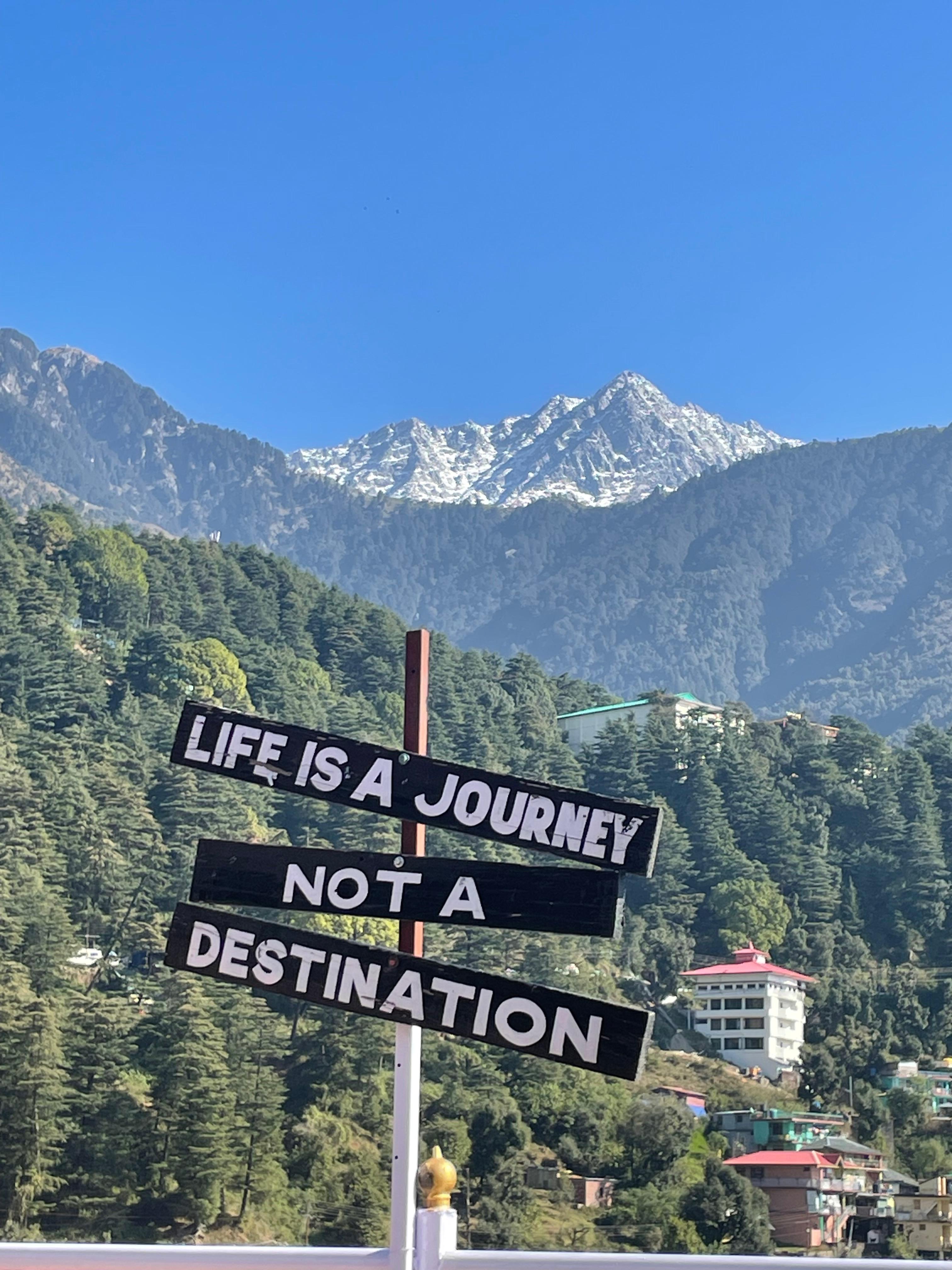 "Life is a Journey" sign at McLeod Ganj with Dhauladhar mountains behind
