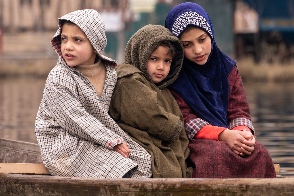 Three Kashmiri children wrapped in woollen pherans seated in a shikara on Dal Lake