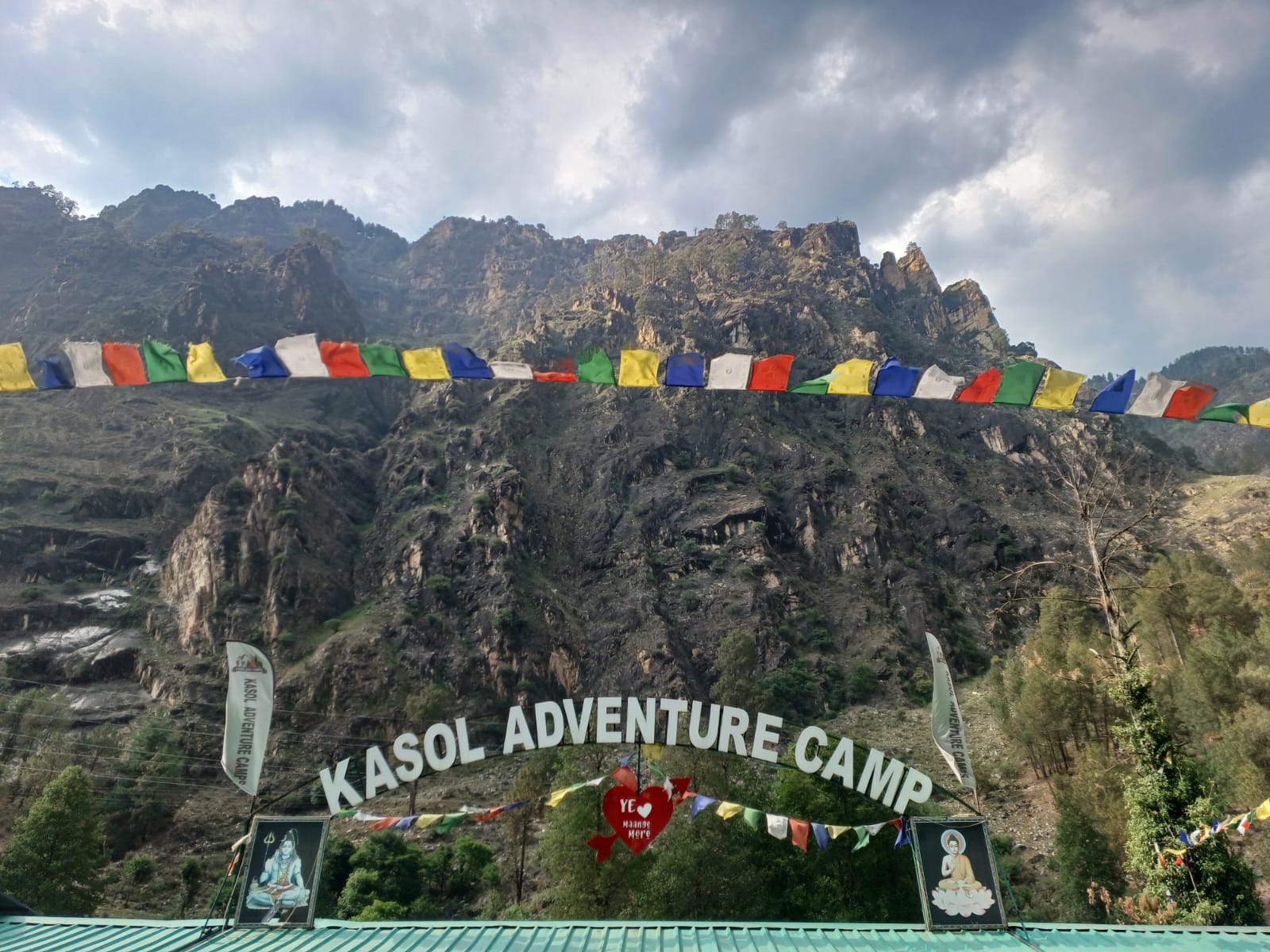 Kasol adventure camp with Tibetan prayer flags and rocky Himalayan peaks above