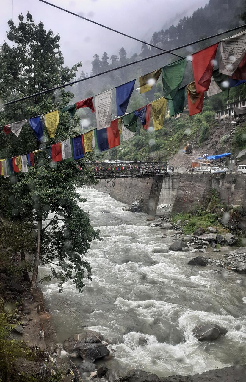 Colourful Tibetan prayer flags strung above the rushing Beas River, Old Manali