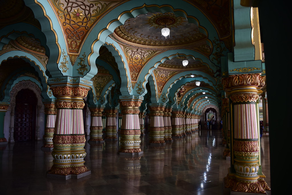 Arched corridor inside Mysore Palace with painted teal ceiling and striped columns