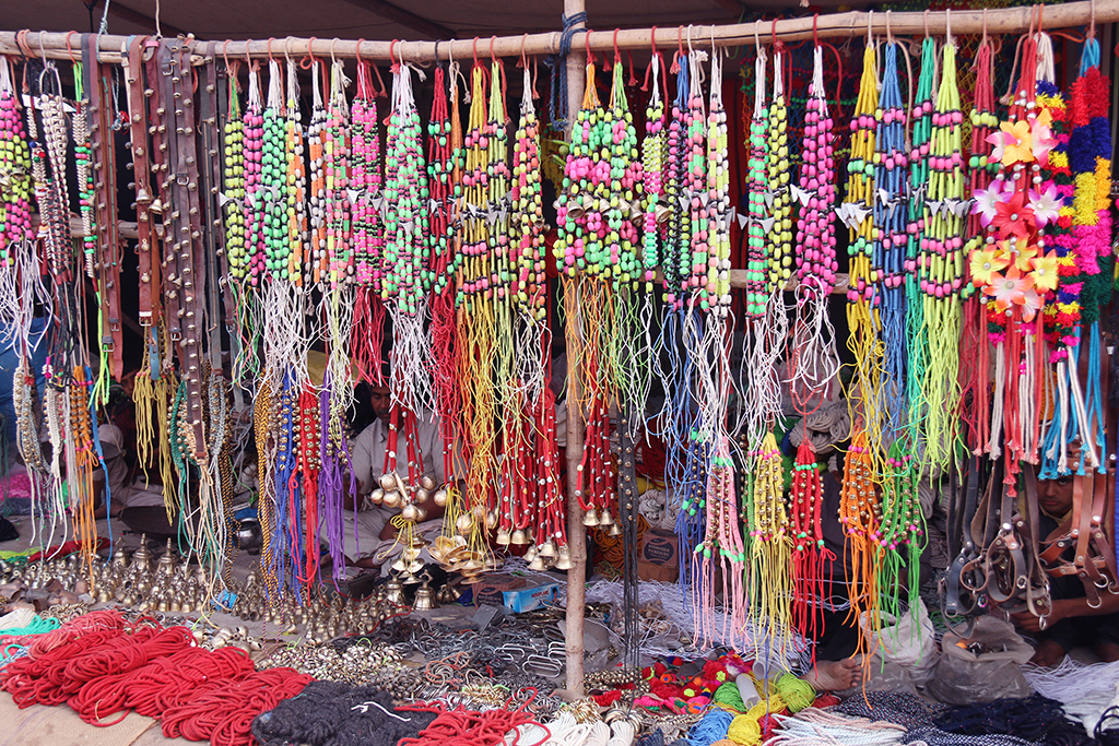 Rows of colourful camel decorations — beaded necklaces, tassels, brass bells and ropes — at a market stall at the Pushkar Camel Fair