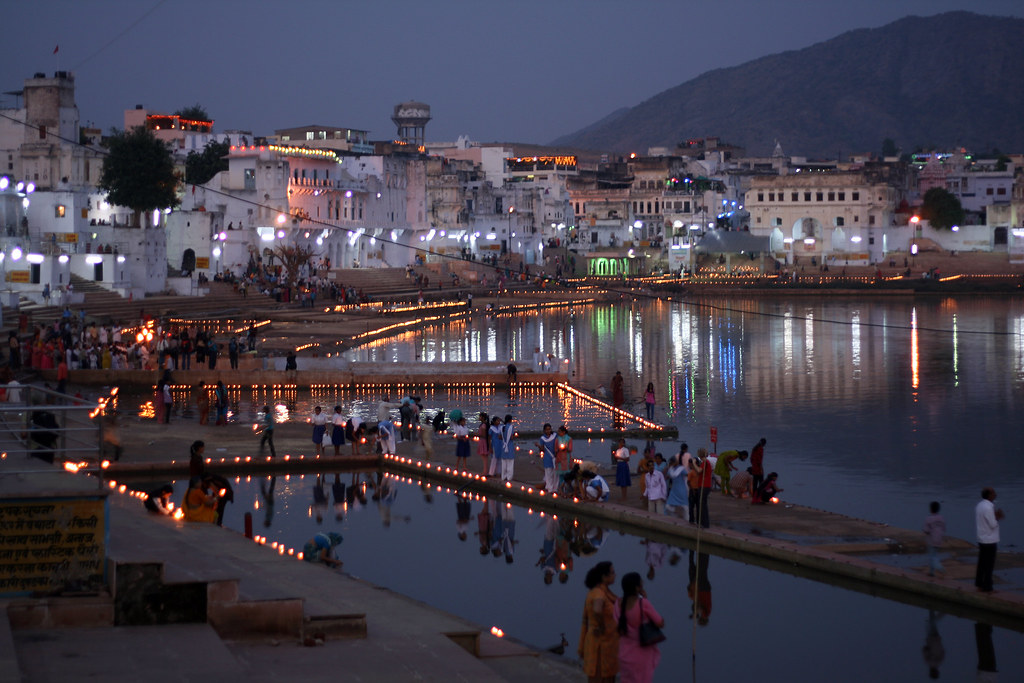 Candlelit ghats at Pushkar Lake at dusk, rows of diyas lining the stone steps and their light shimmering in the still water